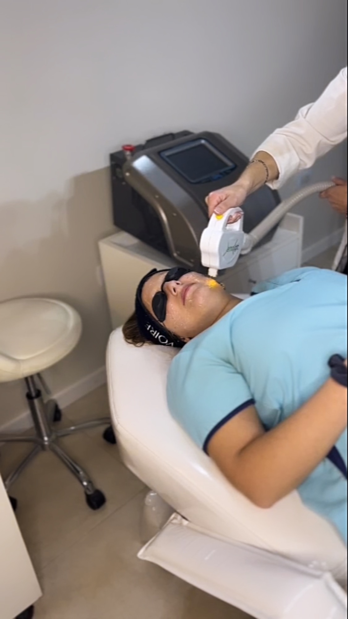 En la cabina del consultorio, una paciente con anteojos protectores recibe un tratamiento facial con un equipo